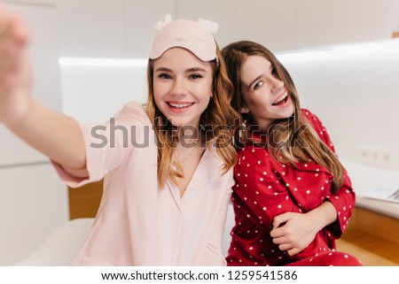 Cute white girl with lovely smile making selfie in light room. Indoor shot of two amazing european ladies enjoying weekend.