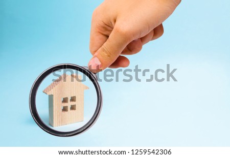 Magnifying glass is looking at the Wooden house on a blue background. The concept of affordable housing and mortgages to buy a house. Buying and selling apartments and property, real estate.