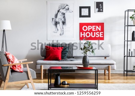 Armchair next to table and grey couch with pillows in living room interior with posters. Real photo