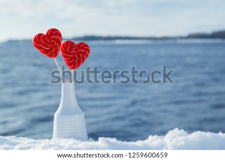 Valentine's day background. Candy hearts in a vase in the snow against the sea or river. Romantic date and Declaration of love on the frosty snowy shore