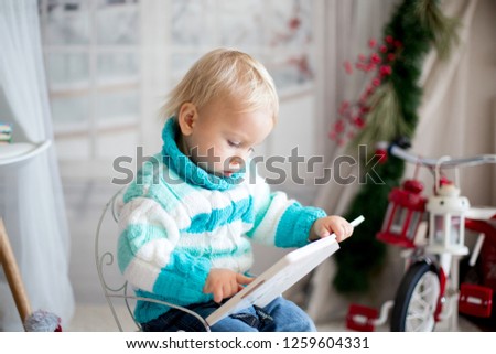 Cute little toddler child with colorful book at home on a snowy winter day, christmas decoration