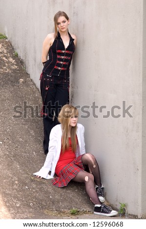 Two attractive teen girls model by a concrete wall, punk and emo fashions.