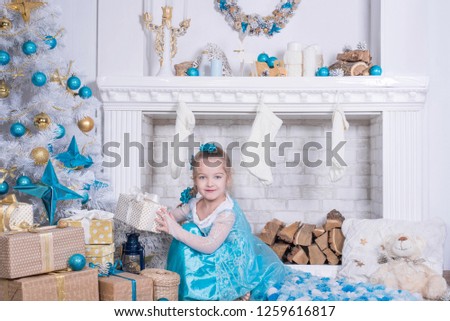 Children at Christmas tree and fireplace on Xmas eve. Family with kids celebrating Christmas at home. girl in blue dress decorating xmas tree and opening presents. Holiday gifts for kid 