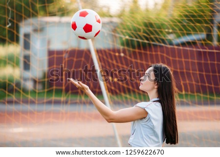 young woman throws soccer ball at stadium on background of grid of football goals