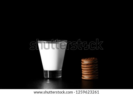 Glass of milk and chocolate cookies on black background.