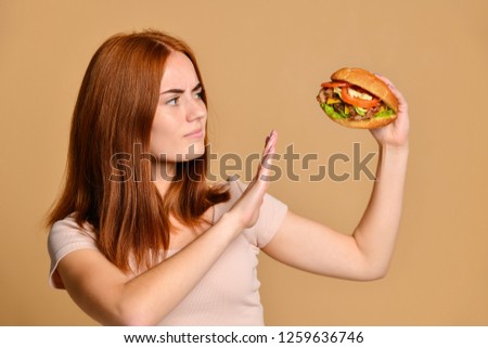 Funny crazy smiling Skinny redhead girl in shorts holds a burger hamburger and refuses to eat it with a gesture of refusal , looking away