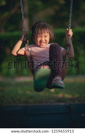 Happy funny a little children girl playing with swing at the playground. Image of emotional cheerful adorable asian kid having fun in summer of outdoors. education activity for kid concept.