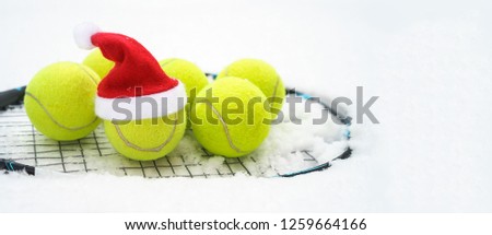 Santa hat on tennis ball, set of tennis balls on racket on white snow winter background. Merry Christmas and New year concept with tennis balls play. Close up, sport lifestyle, funny. Horizontal