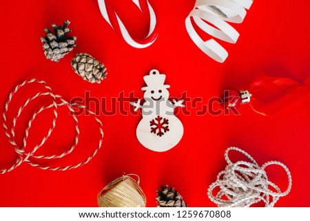 Wooden decoration on the Christmas tree in the form of a snowman on a red background surrounded by Christmas elements. Place for text.