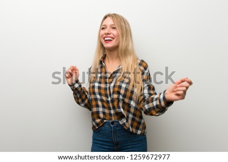 Blonde young girl over white wall enjoy dancing while listening to music at a party