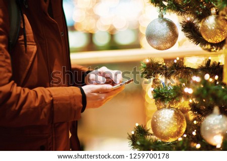 hand using mobile smart phone with colorful light celebration background Man Using Mobile Phone In Room Decorated For Christmas . Guy on the background of Christmas camine. Happy male makes a purchase