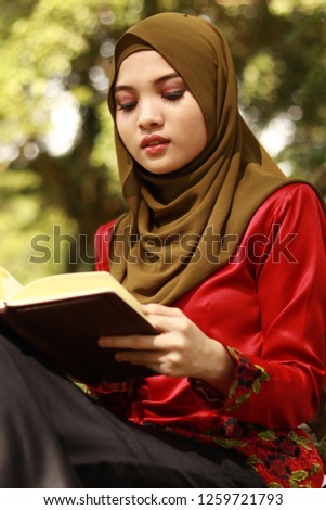 Portrait shot of cute Asian lady wearing hijab holding book.