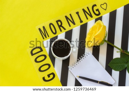 Text Good morning, Cup of coffee, yellow rose and empty notebook for text on stylish black and white napkin on yellow background. Minimal style workplace. Concept good morning. Flat lay Top view 