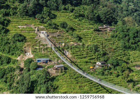 Suspension bridge over the precipice in nepal in middle of the green forest and hills with tradicional houses, Annapurna Circuit trek