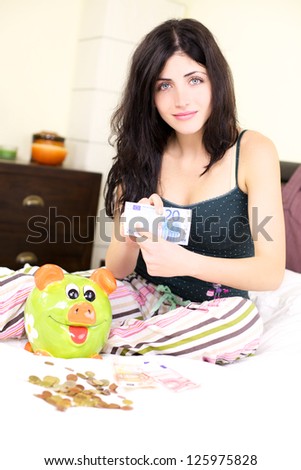 Beautiful young woman holding euros happy about saving in piggy bank for the future