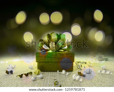 A green gift box with golden ribbon for celebrate Christmas and happy new year  on green fabric, under bokeh yellow lighting on dark background