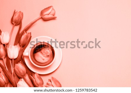 Flat lay of minimalistic picture of cup of coffee and tulips colored in living coral. Trendy color of the year 2019. Minimalism coffee concept.