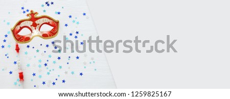 carnival party celebration concept with elegant red mask on stick over white wooden background and stars. Top view