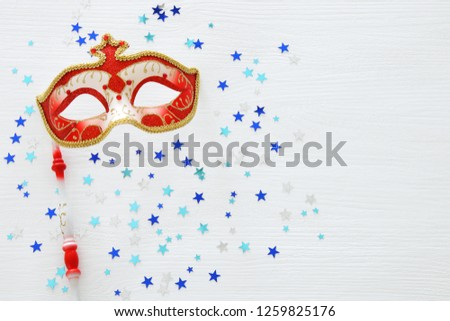 carnival party celebration concept with elegant red mask on stick over white wooden background and stars. Top view