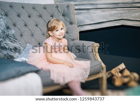 cute girl blonde in a pink dress on a gray sofa, Christmas and warm New Year's photo