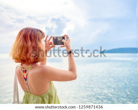 Beautiful asian woman with short hair using smartphone take a photo seascape view with copy space.