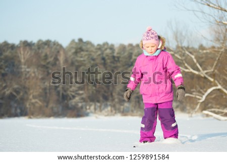 Girl 6 years old riding cross-country skiing without sticks. Purple costume. Sunny day. In the background is a forest.