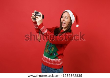 Excited Santa girl keeping mouth wide open doing taking selfie shot on retro vintage photo camera isolated on red background. Happy New Year 2019 celebration holiday party concept. Mock up copy space