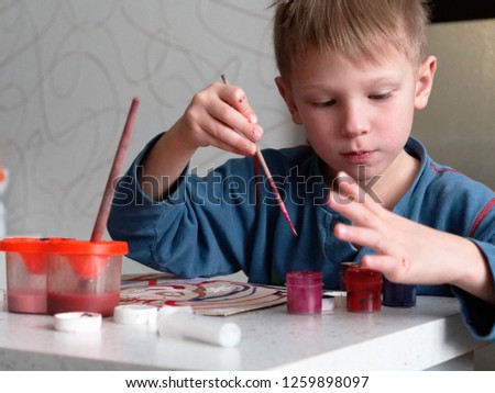 child boy enthusiastically paints with watercolors on paper.