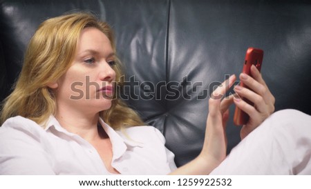 close-up. Elegant woman in a white suit sits in a large black leather chair, and uses her red smartphone. copy space