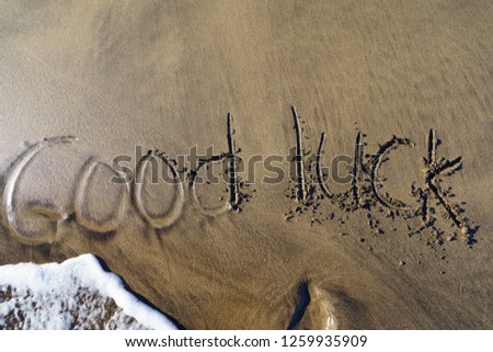 The picture on the sand in the Crand Canaria beach. Ocean wave washing away the inscription "Good luck"
