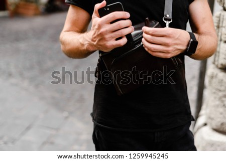Male hands with black digital watch and smartphone. Man wearing black shirt outdoors.