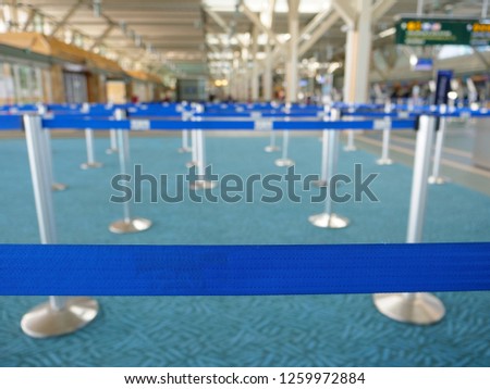 CLOSE UP, DOF: Empty baggage drop lines inside a bright international airport. Blurred shot of a the airport terminal behind the bright blue barriers creating lines in front of the check in counters.