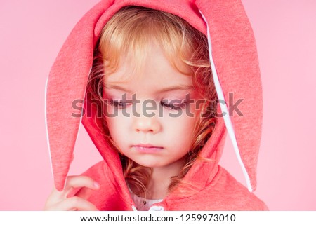 beautiful charming little girl curly blonde hairstyle wearing red sweater clothes with hood rabbit ears.Adorable child celebrate Easter,playing theater role of the easter bunny pink background studio