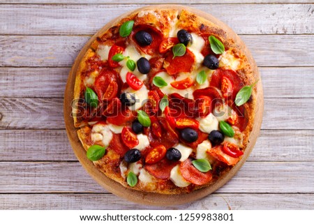 Delicious pizza served on wooden plate. Pizza with pepperoni, tomatoes, cheese, olives and basil. View from above, top studio shot