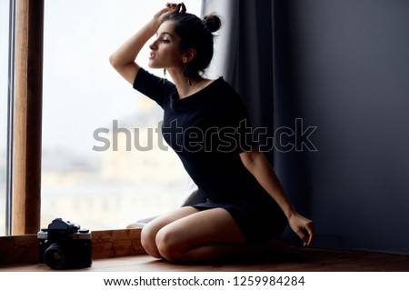 A woman in a short dress is sitting on the window sill near the window                       