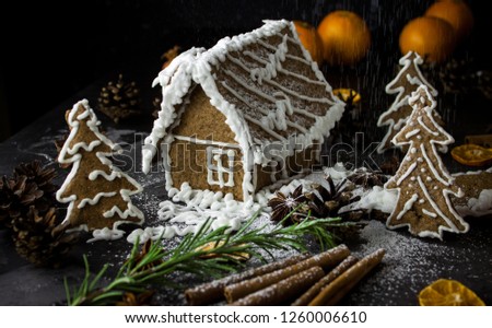 Homemade gingerbread house on black night background, ginger cookies. Christmas dark photo. Tangarines, anis stars, cinnamon sticks and cones. Sweet winter ginger cookies picture.
