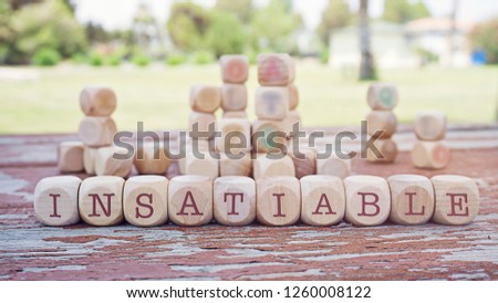 Insatiable word written on cube shape wooden blocks on wooden table.