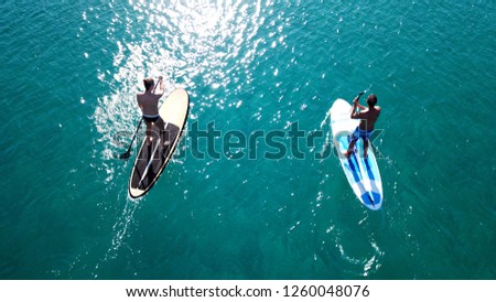 Aerial photo of 2 fit men practising SUP or STand Up Paddle board in tropical turquoise sea