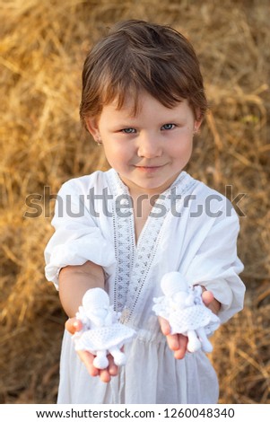 Little girl showing knitted angels. Vertical photo. 
