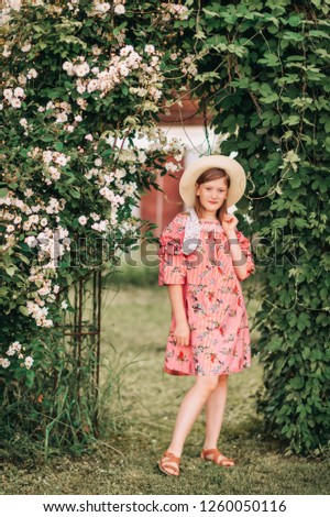 Summer portrait of pretty little girl wearing red stripe dress, posing in rose garden