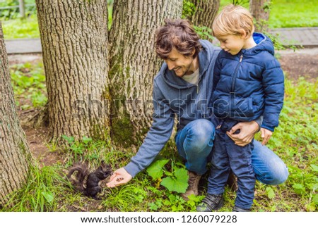 Dad and son feed a squirrel in the park
