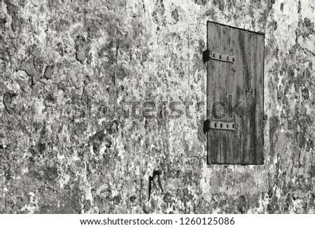 Window with closed wooden shutter on the weathered stone facade of abandoned rural house. Grunge background. Decay despair concept. Black and white photo.