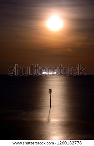 Full moon and sea reflections over Sandown Bay on the Isle of Wight with breakwater and ship on the horizon.
