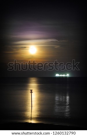 Full moon and sea reflections over Sandown Bay on the Isle of Wight with breakwater and ship on the horizon.