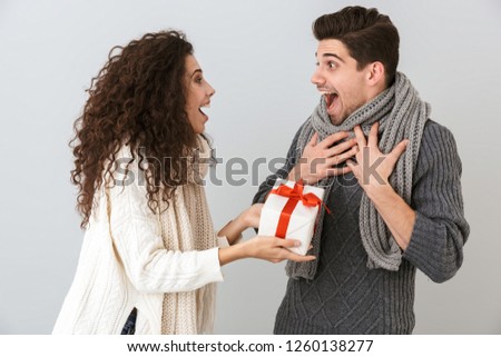 Image of surprised man and woman rejoicing while standing with present box isolated over gray background