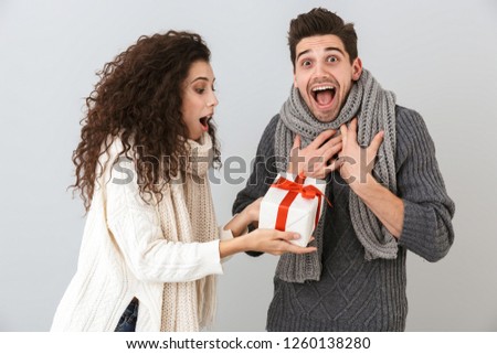Image of caucasian man and woman rejoicing while standing with gift box isolated over gray background