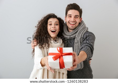 Image of beautiful man and woman rejoicing while standing with present box isolated over gray background
