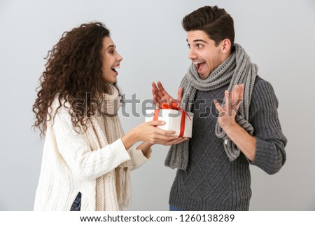 Image of pleased man and woman rejoicing while standing with present box isolated over gray background
