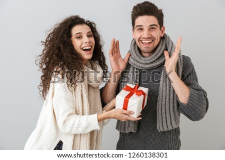 Image of attractive man and woman rejoicing while standing with present box isolated over gray background