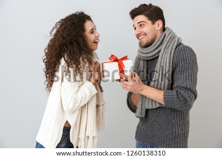 Image of young man and woman rejoicing while standing with present box isolated over gray background